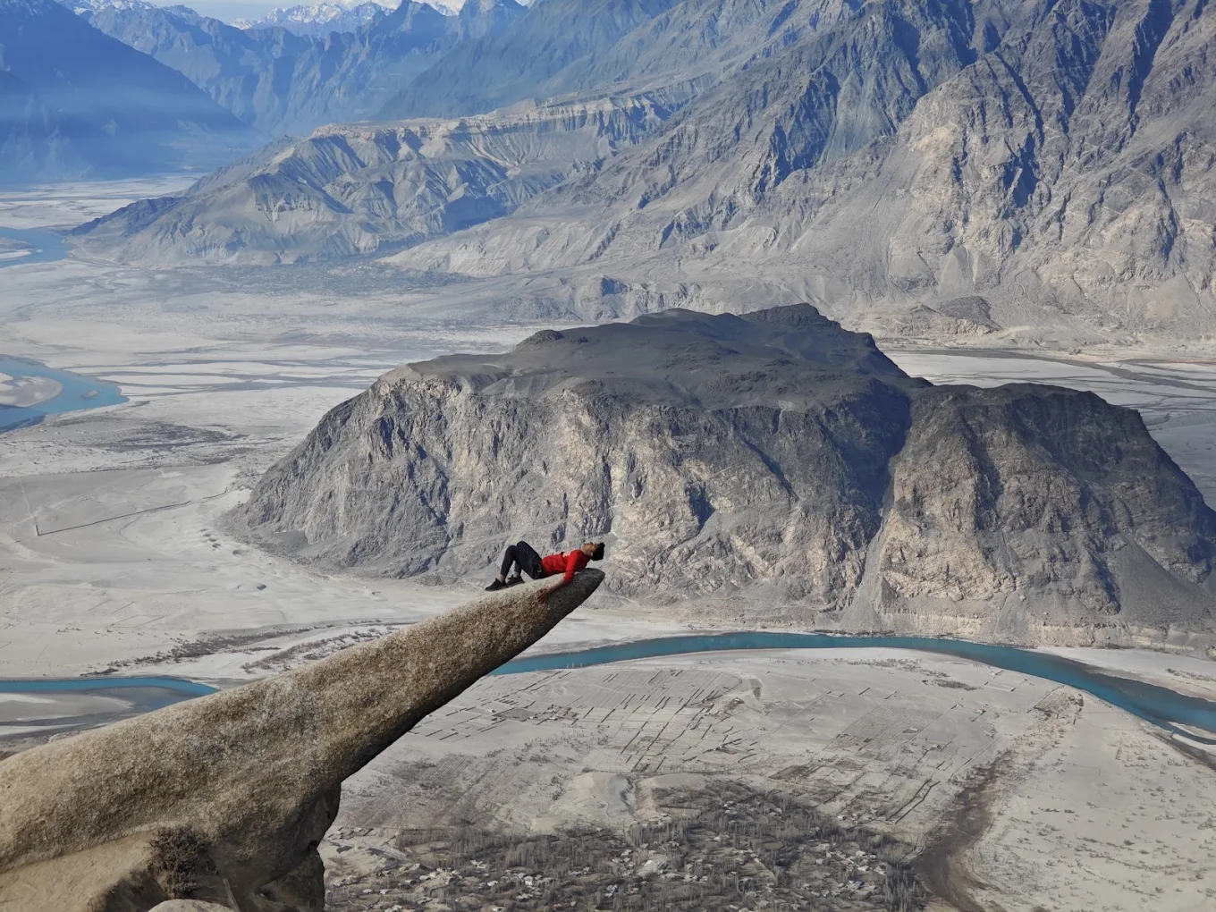 A hiker lying on the Marsur Rock ledge above the Skardu valley, Indus River and Karakoram mountains